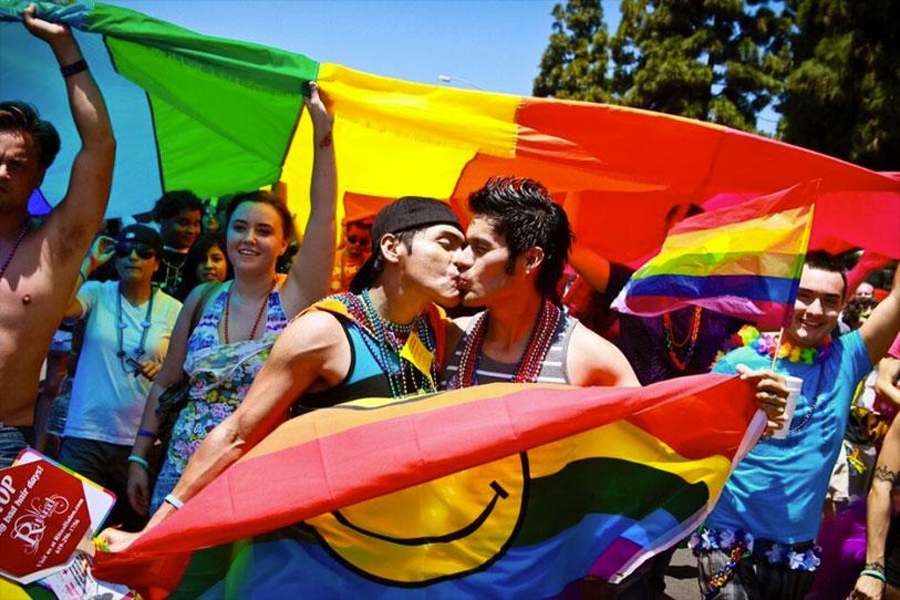 Gay pride parade showing two men kissing holding a rainbow flag